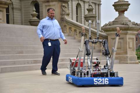 A middle aged man looking at a robot and smiling