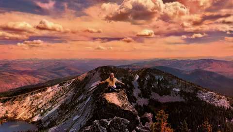 Teen girl sitting on a mountain peak during sunset