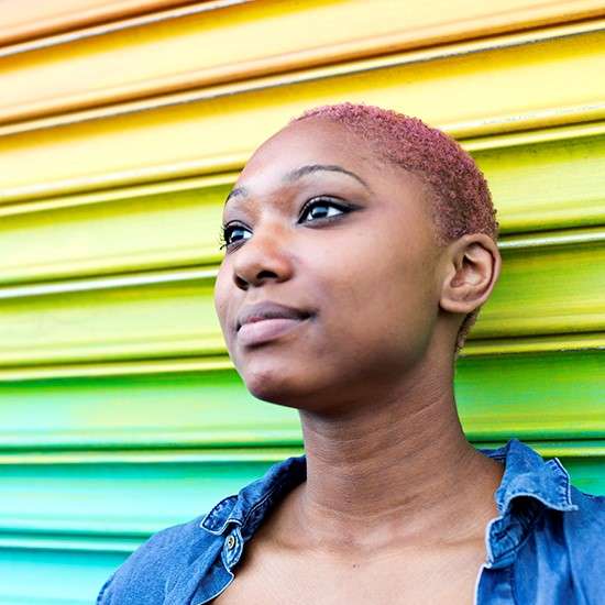 Teen leader stands against rainbow wall and smiles toward the sky.