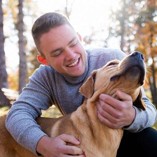 Teen smiles while outside playing with their dog.